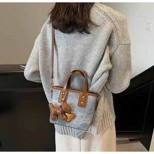 Vue détaillée d'un sac seau en denim bleu avec garniture en cuir brun et bijou de sac