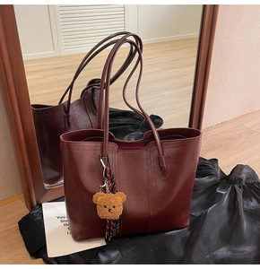 Detail of dark red faux leather tote bag with plush bear charm and striped ribbon accent
