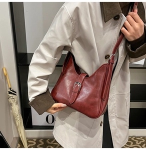 Détail d'un sac seau vintage rouge foncé porté sur un manteau beige élégant