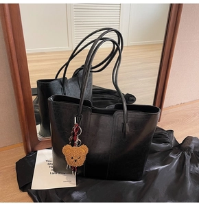 Detail of black faux leather tote bag featuring a cute brown plush bear charm pendant