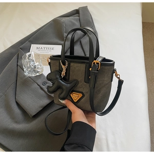 Détail du sac seau en toile avec finitions cuir et pendentif chien sur un blazer gris