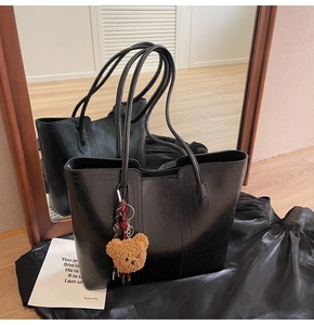 Close-up of black leather tote bag featuring vertical seams and a cute brown plush bear charm