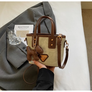 Détail du sac seau en toile beige et cuir marron avec poignées et plaque de logo