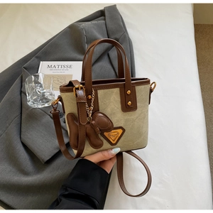 Détail du sac seau en toile avec bordure en cuir marron et breloque chiot suspendue