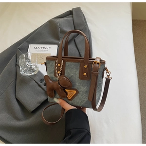 Détail d'un sac seau en toile avec bordure en cuir et breloque chiot sur un blazer gris