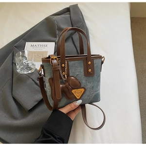 Détail du sac cabas en denim bleu avec garniture en cuir marron et breloque chiot