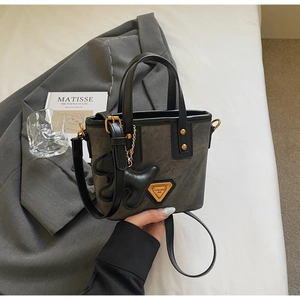 Détail du sac seau gris texturé avec poignée en cuir noir et logo doré sur un costume