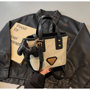 Détail du sac seau en toile beige avec bordure en cuir noir et breloque petit chien