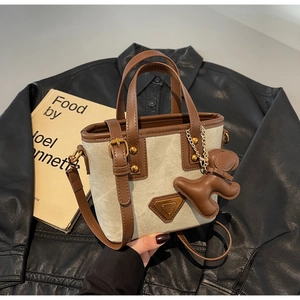 Détail du sac cabas en toile avec garniture en cuir marron, logo en métal et breloque