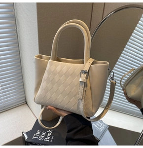 Detailed view of beige bucket bag with quilted texture and adjustable strap on a mirror