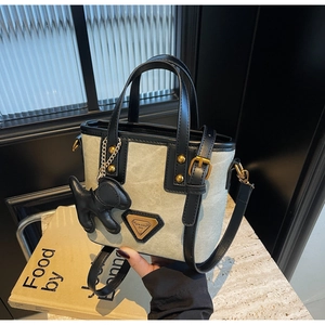 Détail du sac seau en toile crème avec finitions en cuir noir et logo doré triangulaire