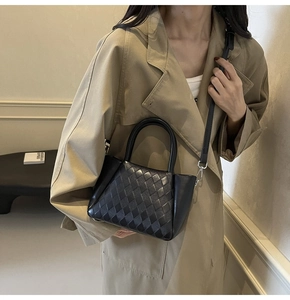 Detail of a black woven crossbody bag with silver hardware on a khaki trench coat