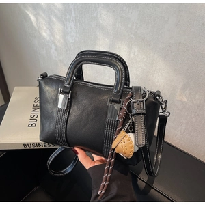 Détail du sac Boston en cuir noir avec surpiqûres blanches et breloque gant de baseball