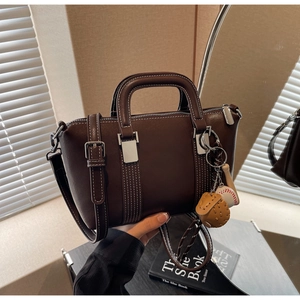 Détail d'un sac en cuir marron avec surpiqûres blanches et pendentif de baseball