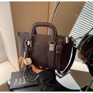 Détail du sac Boston en cuir marron foncé avec coutures contrastées et breloque baseball