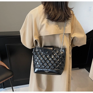 Quilted black bucket bag with silver chain and white fashion text shown on a beige trench coat