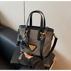 Détail du sac seau en toile grise avec bordure en cuir noir et breloque chiot