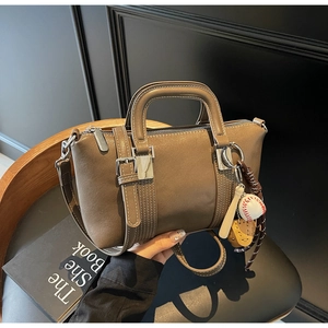 Détail du sac à main en cuir beige avec coutures blanches et breloque sport sur une chaise