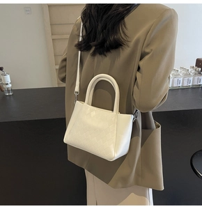 Detail of white quilted crossbody bag with top handles and silver metal hardware