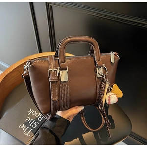 Détail d'un sac à main marron avec surpiqûres blanches et breloque baseball