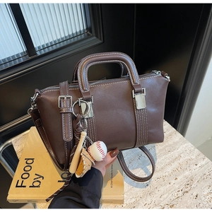 Détail du sac à main en cuir marron foncé avec surpiqûres et charm de baseball