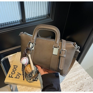 Détail du sac Boston marron foncé avec breloques de baseball et coutures texturées