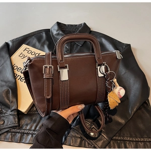 Détail du sac à main en cuir marron foncé avec surpiqûres et breloque de baseball