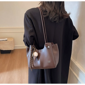 Detail of dark brown leather tote bag featuring metal logo and cute plush ball charm