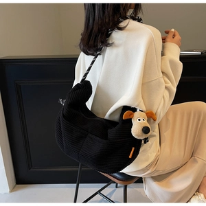 Detail of black corduroy crossbody bag with striped strap and plush puppy charm