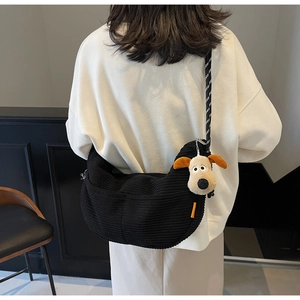 Detail of black corduroy crossbody bag with woven strap and cute plush dog charm