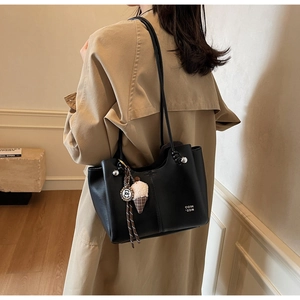 Detail of black leather tote bag featuring white logo print and creative plush charm