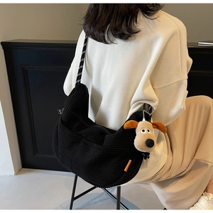 Detail of black corduroy hobo bag with a checkered strap and cute puppy pendant