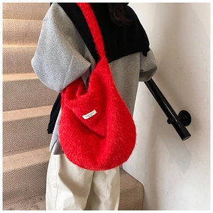 Detailed view of a red plush hobo tote bag worn by a model in an urban outdoor setting