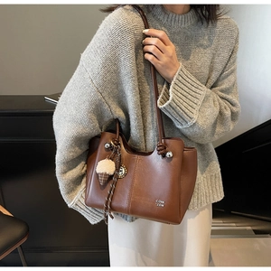 Detail of dark brown leather tote bag featuring a plush charm and fine vertical stitching