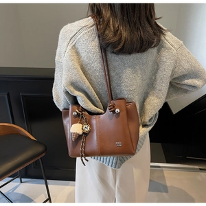Detail of a dark brown leather tote bag with knotted slim straps and ice cream charm