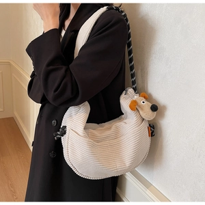 Detail of beige corduroy crescent bag with woven strap and plush puppy charm decor
