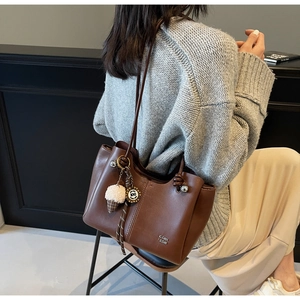 Detail of brown leather tote bag featuring a plush charm and metal logo on smooth PU surface