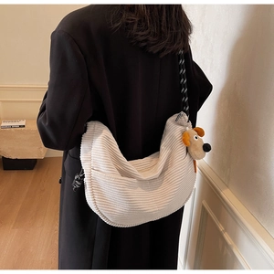 Detail of cream corduroy crescent bag with rope strap and plush dog charm worn by a model