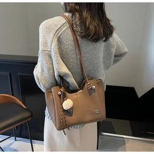 Detail of a brown leather tote bag with ice cream plush charm and metal logo on strap