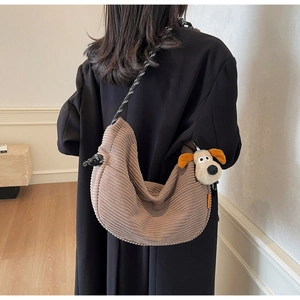 Detail of brown corduroy crescent bag featuring a woven strap and plush dog pendant