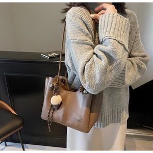 Detail view of brown leather tote bag with vertical stitching and plush ice cream charm