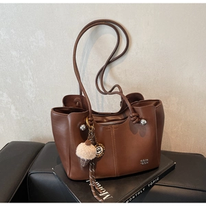 Close-up of deep brown tote bag with metal logo, long straps and plush ice cream charm