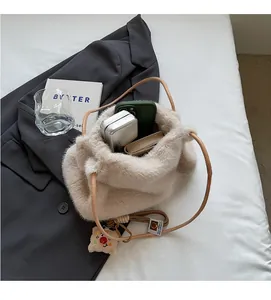 Dettaglio della borsa a secchiello in peluche beige con texture morbida e ciondolo