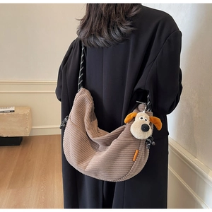 Brown corduroy dumpling bag with woven strap and plush puppy charm worn by a model