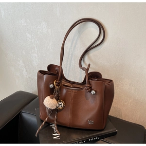 Detail of brown leather tote bag featuring vertical stitching and a plush ice cream charm