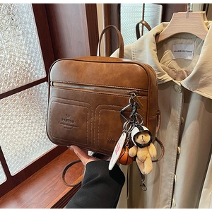 Detail of vintage brown leather backpack featuring embossed text and cute hanging charms