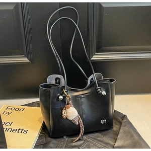 Detail of a black leather tote bag featuring a plush charm and slender double shoulder straps