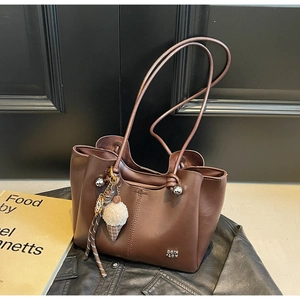 Detail of brown tote bag with metal logo and plush ice cream charm on leather clothes