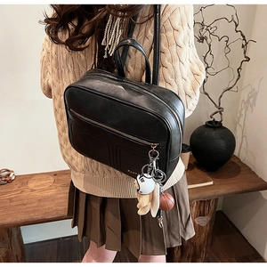Detail of black leather backpack with decorative plush charms and zipper front pocket