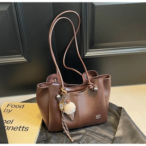 Detail of dark brown leather tote bag with metal logo and ice cream charm accessory